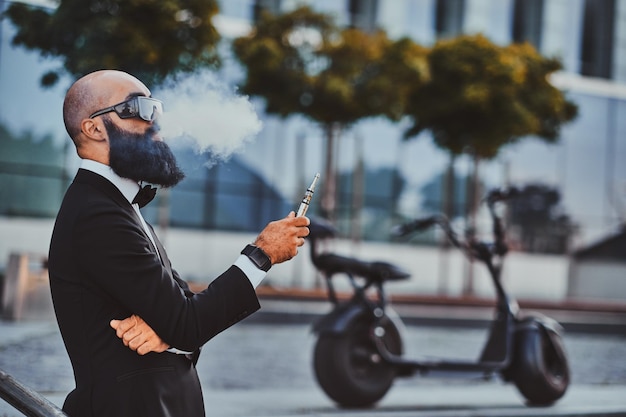 Nachdenklicher, eleganter Geschäftsmann mit Sonnenbrille raucht Verdampfer und macht schöne Wolken.