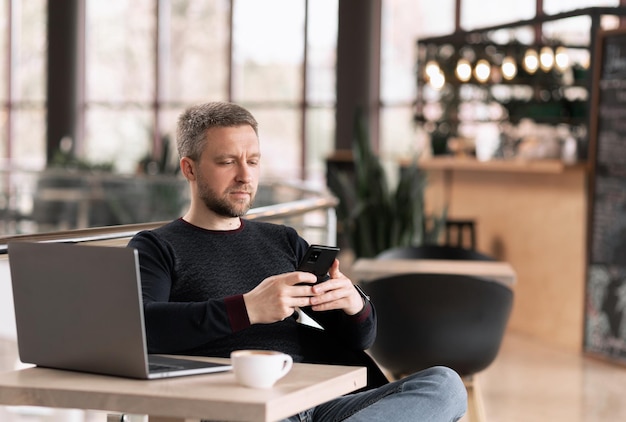 Nachdenklicher Geschäftsmann trinkt Kaffee in einem Café und schaut auf das Telefon