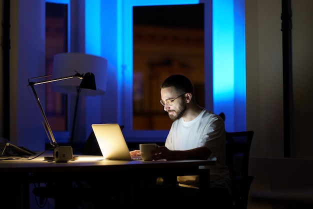 Nachdenklicher junger Geschäftsmann mit Brille arbeitet nachts am Laptop und bereitet sich auf die Startpräsentation vor