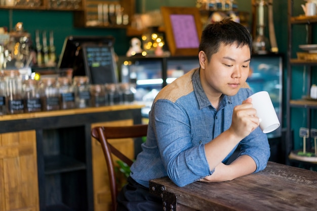 Nachdenklicher junger Mann, der Unterseite des Bechers beim Stillstehen in der Kaffeestube betrachtet.