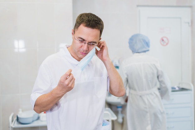 Nachdenklicher männlicher Chirurg, der chirurgische Maske im Krankenhaus trägt