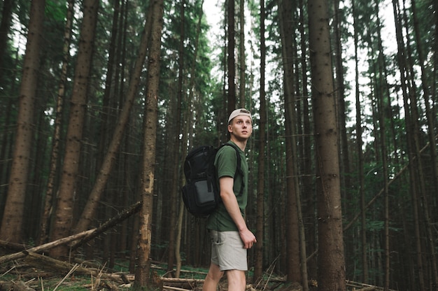 Nachdenklicher männlicher Wanderer mit einem Rucksack, der im Nadelwald steht und weit nach vorne schaut
