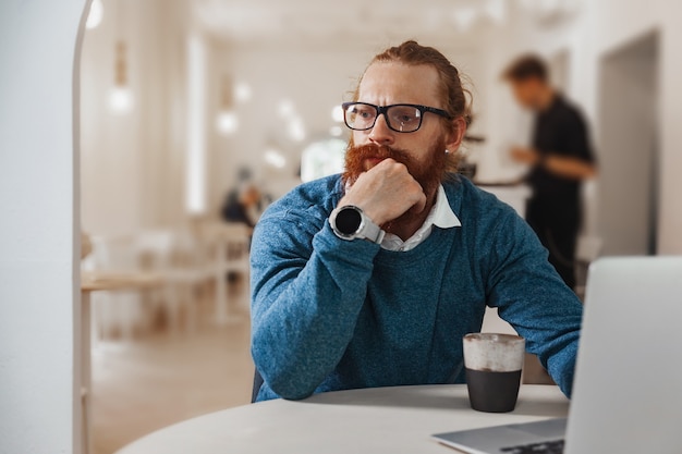 Nachdenklicher rothaariger Mann, der an Laptop im Café arbeitet