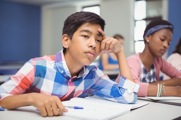 Nachdenklicher Schüler, der im Klassenzimmer sitzt