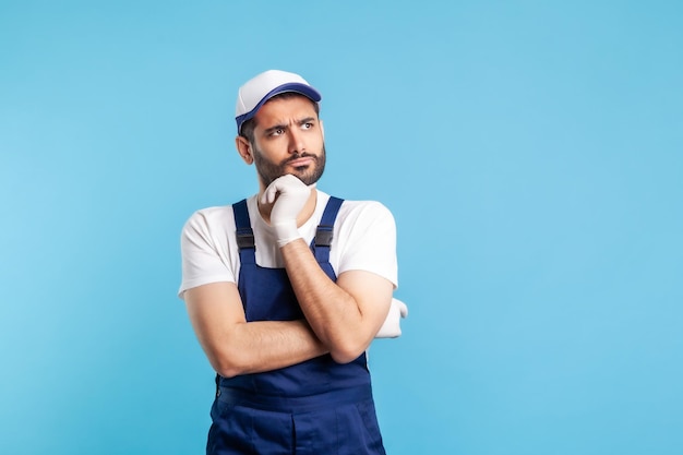 Nachdenklicher verwirrter Handwerker in Overalls, der das Kinn hält und über Entscheidungen nachdenkt, die Verdacht haben und an der Wahl zweifeln Beruf der Dienstleistungsbranche Kurierdienst Hauswirtschaft isoliert