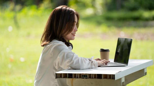 Nachdenkliches Lächeln Glückliche Frau, die online Videoanrufe macht oder online mit einem Laptop in einem Park arbeitet