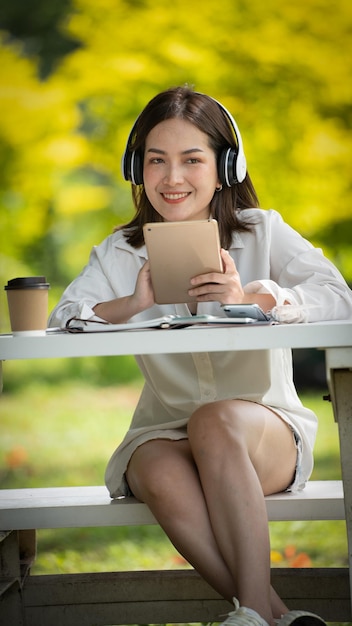 Nachdenkliches Lächeln Glückliche Frau, die online Videoanrufe macht oder sich online trifft und mit einem Tablet in einem Park arbeitet