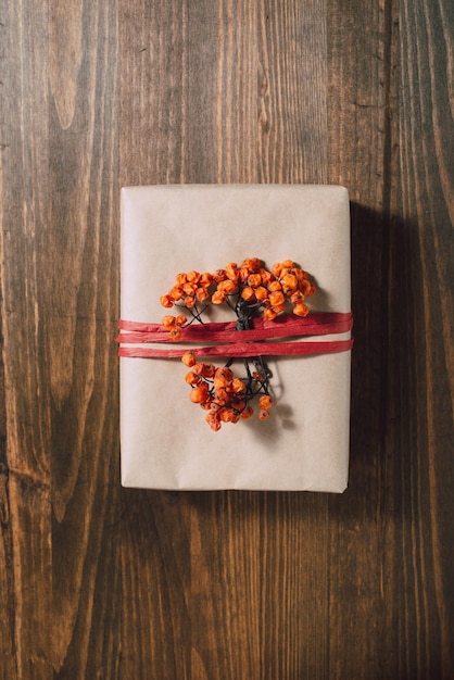 Nachhaltige Geschenkverpackung Flachgelegte Geschenkbox verpackt und dekoriert mit Kraftpapierband und getrockneten Beeren auf Holztisch