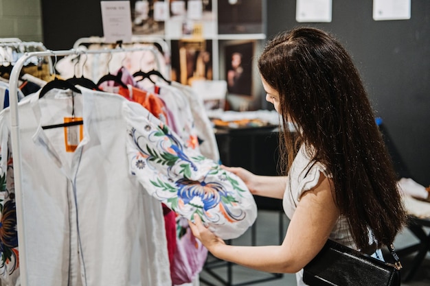 Nachhaltige Mode junge Latina junge Frau wählt ethnische Boho-Kleidung im Vintage-Shop