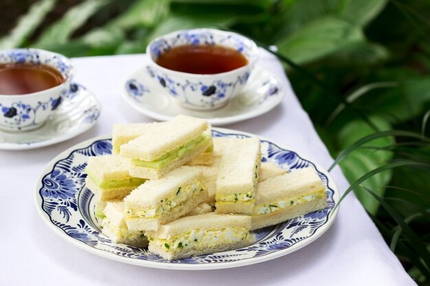 Nachmittagstee im Garten, Fingersandwiches mit Gurken- und Eiersalat und Tee auf einem Licht.