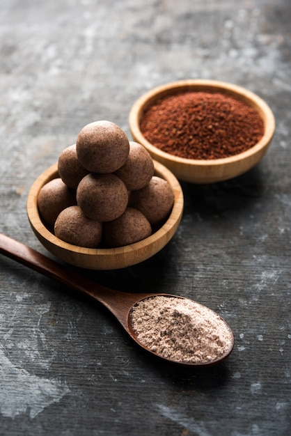 Nachni laddu o Ragi laddoo o bolas hechas con mijo, azúcar y ghee. Es un alimento saludable de la India. Servido en un bol o plato con crudo entero y en polvo. Enfoque selectivo