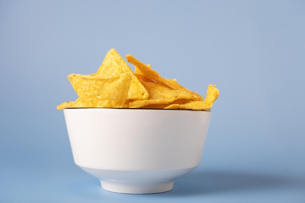 Nacho chips de milho em uma tigela branca sobre um fundo azul