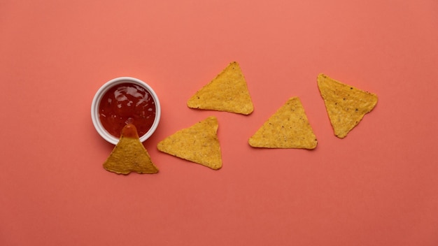 Nachos-Chips in Sauce auf farbigem Hintergrund