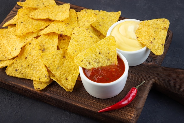 Nachos de chips de maíz mexicano con salsas sobre tabla de cortar rústica.