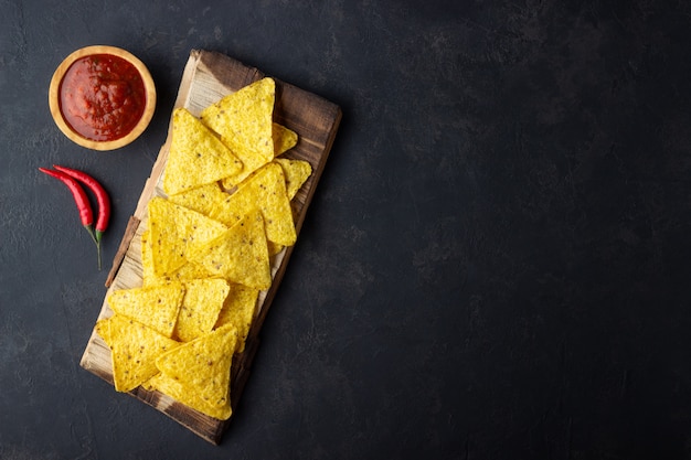 Nachos de chips de milho de comida mexicana tradicional com molho de salsa em fundo preto. Vista superior com espaço de cópia.