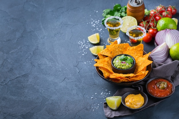 Nachos de tortilla de milho amarelo com guacamole, molho de pimenta jalapeño e molho de queijo com tequila em uma mesa escura. Copie o fundo do espaço