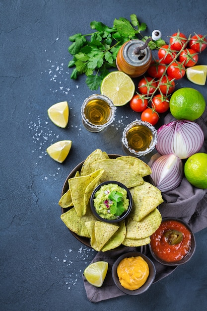 Nachos de tortilla de milho amarelo com guacamole, molho de pimenta jalapeño e molho de queijo com tequila em uma mesa escura. vista superior do plano de fundo