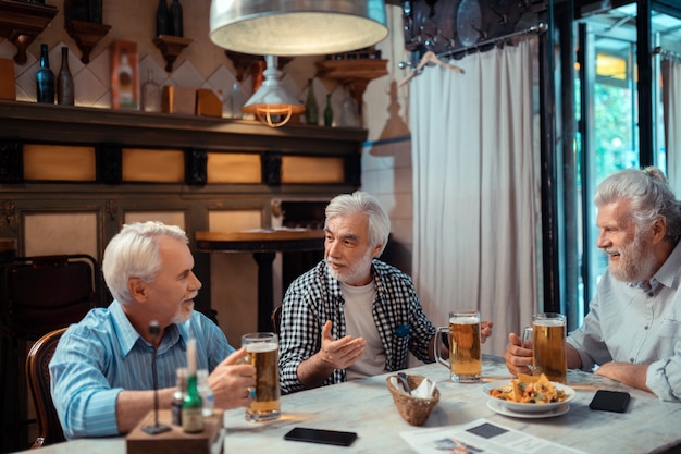 Nachos e cerveja. Três aposentados alegres e positivos comendo nachos e bebendo cerveja