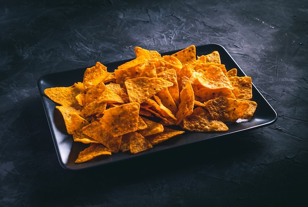 Nachos in einem dunklen rechteckigen Teller auf einem dunklen Tisch