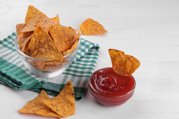 Nachos in einer Schüssel mit roter Sauce auf einem weißen Holztisch