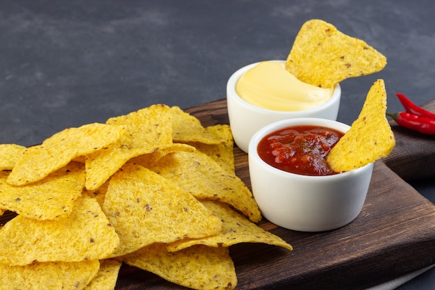 Nachos mexicanos de chips de milho com molhos em tábua rústica.