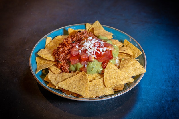 Nachos mit Guacamole und Tomatensauce auf schwarzem Hintergrund, auf blauem Teller