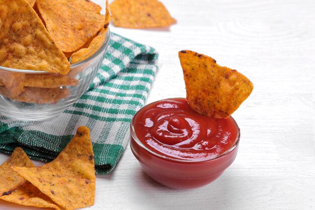 Nachos en un recipiente con salsa roja sobre una mesa de madera blanca