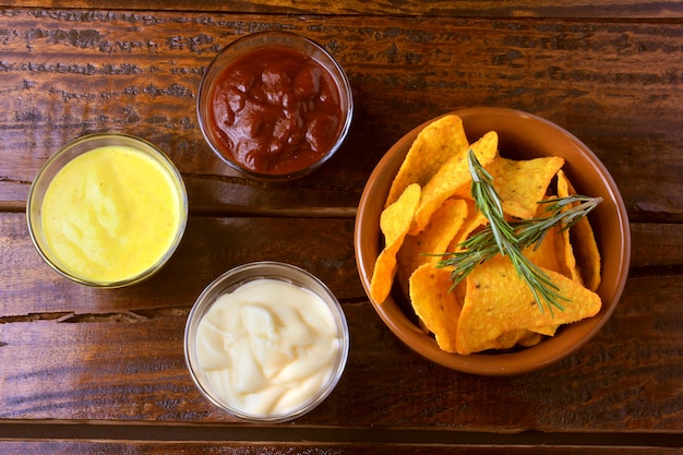 Nachosmaischips platziert in Keramikschale auf Holztisch neben sortierten Soßen