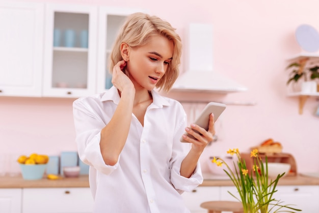 Nachricht lesen. Junge blonde Frau mit schönem natürlichem Make-up liest Nachricht vom Freund