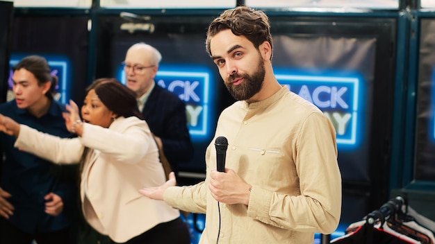 Nachrichtenreporter in überfülltem Bekleidungsgeschäft hält Mikrofon in der Hand und sendet verrücktes Verhalten am Black Friday. Fernsehjournalist erstellt Live-Nachrichtensendung vor Ort im örtlichen Einkaufszentrum.