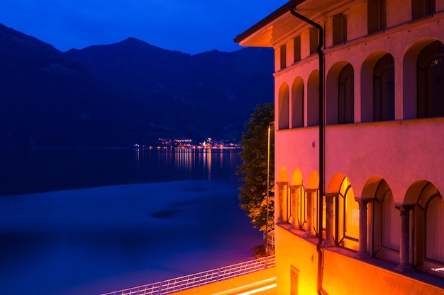 Nacht italienische Stadt: ein Gebäude mit beleuchteten Bögen und Blick auf den See.