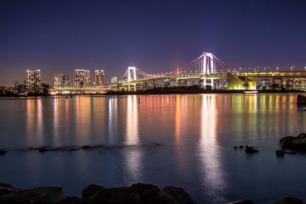 Nachtansicht der Regenbogenbrücke mit Reflexion in der Bucht von Tokyo.