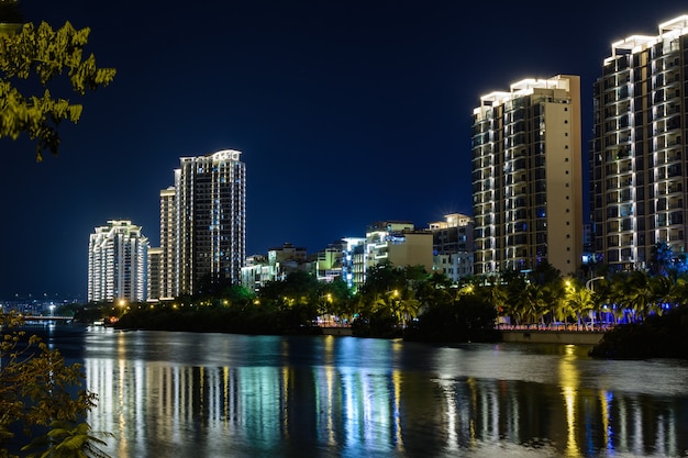 Nachtansicht der Stadt Sanya mit hellen mehrfarbigen Beleuchtungsgebäuden, Strukturen, Straßen, Bürgersteigen, Masten, Brücken. Sanya, Hainan, China