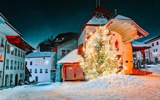 Nachtansicht des beleuchteten Weihnachtstannenbaums auf der Straße. Freiburg im Winter. Schweiz. Greyerzer mit Schnee. Schloss in der Nähe von Charmey Europe. Schweizer Traditionsdorf zu Weihnachten oder Neujahr