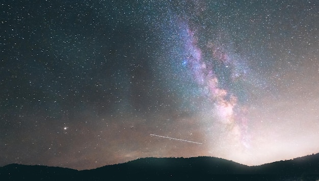 Nachtlandschaft mit bunter Milchstraße und gelbem Licht an den Bergen. Sternenhimmel mit Hügeln. Schönes Universum.