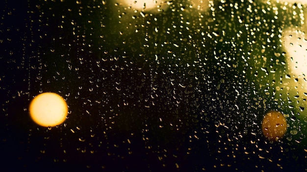 Nachts Regentropfen am Fenster. Eigentumswohnung oder Wohnung Wohnzimmerfenster in der Nacht der Regenzeit in Bangkok Thailand. Das Außenfenster ist verschwommenes Bokeh aus regnerischem Stadtlicht und natürlichem Baum und Himmel.