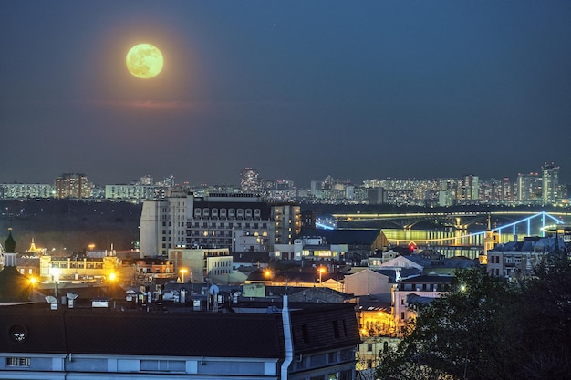 Nachtstadtbild mit großem Vollmond über Podil Kiew in der Ukraine, Stadtlichter und Blick auf die Brücke