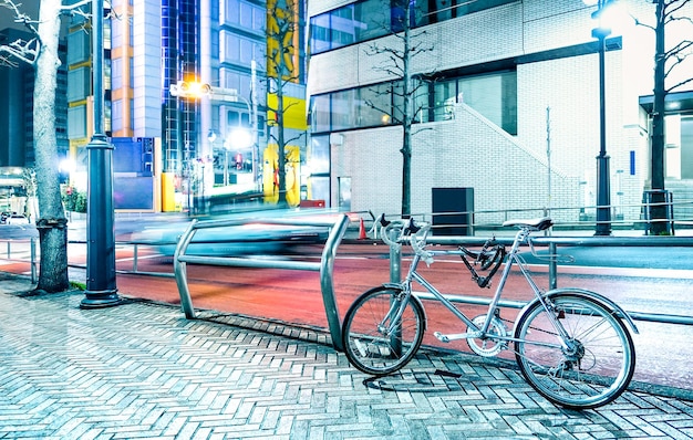 Nachtszene mit geparktem fahrrad und unscharfem, schnell fahrendem auto im stadtzentrum von tokio