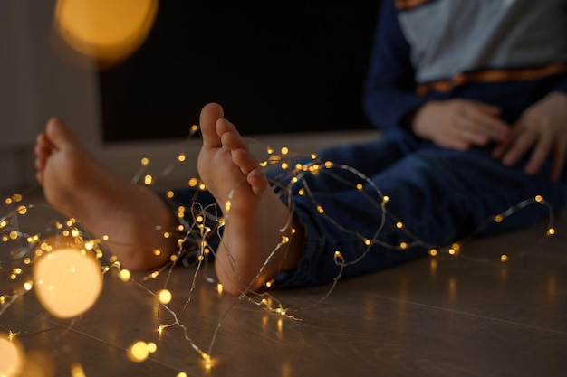 nackte Füße eines Jungen in Jeans und einem Pullover mit einer Weihnachtsgirlande