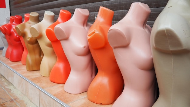 Nackte Plastikpuppen in Beige, Rosa, Rot und Orange stehen vor einem Schaufenster Frauentorsi ohne Arme und Köpfe Outlet-Ausstattung Handelsplatz Bunte Dummies