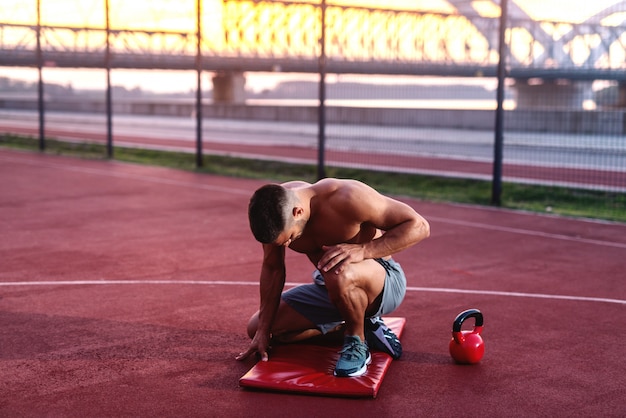Nackter Oberkörper muskulöser Mann kniet und posiert am Morgen auf dem Platz.