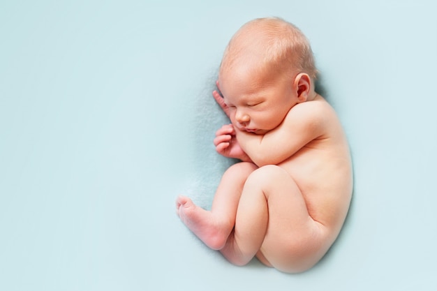 Nacktes neugeborenes Baby, das auf dem blauen Hintergrund schläft