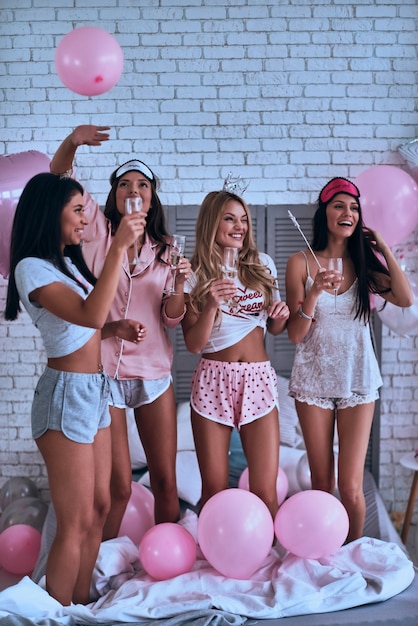 Nada é melhor do que amigos. Comprimento total de quatro mulheres atraentes e sorridentes de pijama bebendo champanhe durante uma festa do pijama