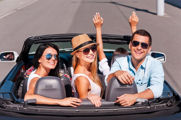 Nada más que amigos y viaje por carretera. Vista superior de jóvenes felices disfrutando de un viaje por carretera en su convertible blanco y sonriendo