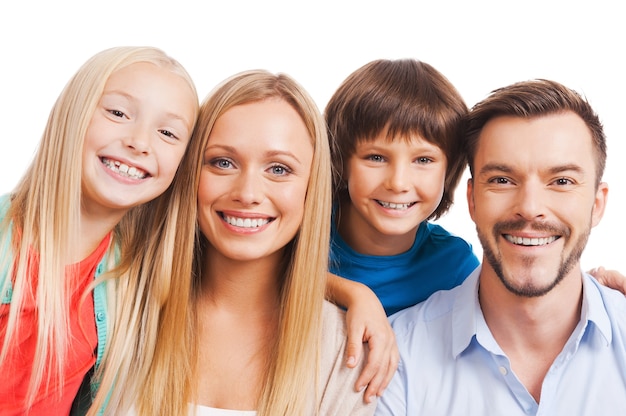 ¡Nada más que familia! Feliz familia de cuatro pegados entre sí y sonriendo mientras está de pie contra el fondo blanco.