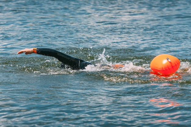 Nadador atleta en traje de neopreno con boya nadando en el agua