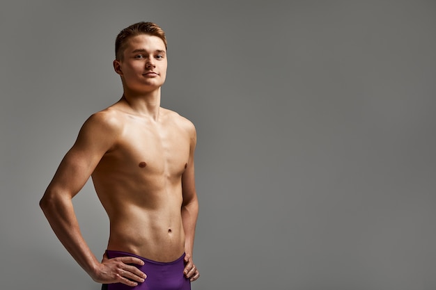 Foto nadador de jovem atleta em excelente forma física olha para a câmera, retrato de meio comprimento em um fundo cinza, cópia espaço, motivação para esportes, banner publicitário.