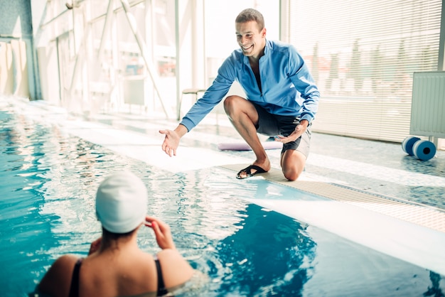 Nadador feminino no exercício cap com personal trainer masculino na piscina coberta.