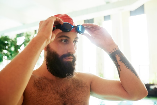 Un nadador con gorra y gafas se pone gafas de natación sonriendo antes de entrenar en la piscina