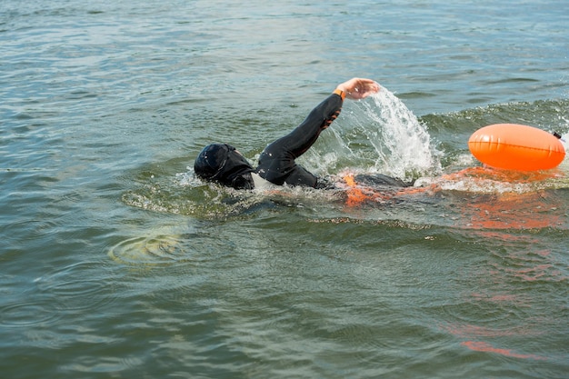 Un nadador en traje de neopreno con una boya nada en el agua del río.